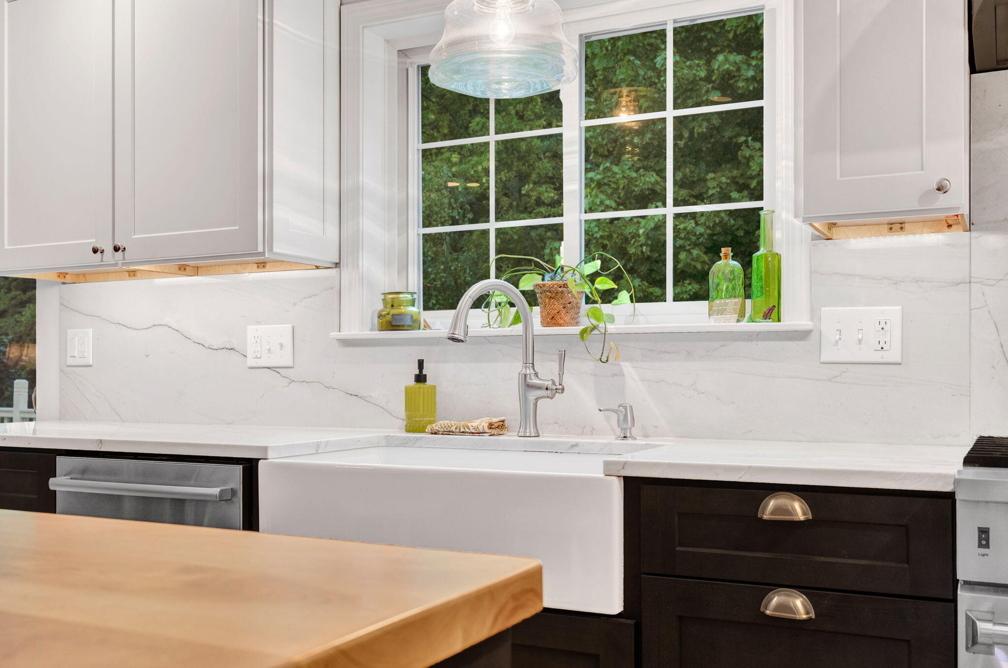 Kitchen sink beneath a large window, with marble-look counters, dark cabinets, and a wood island.