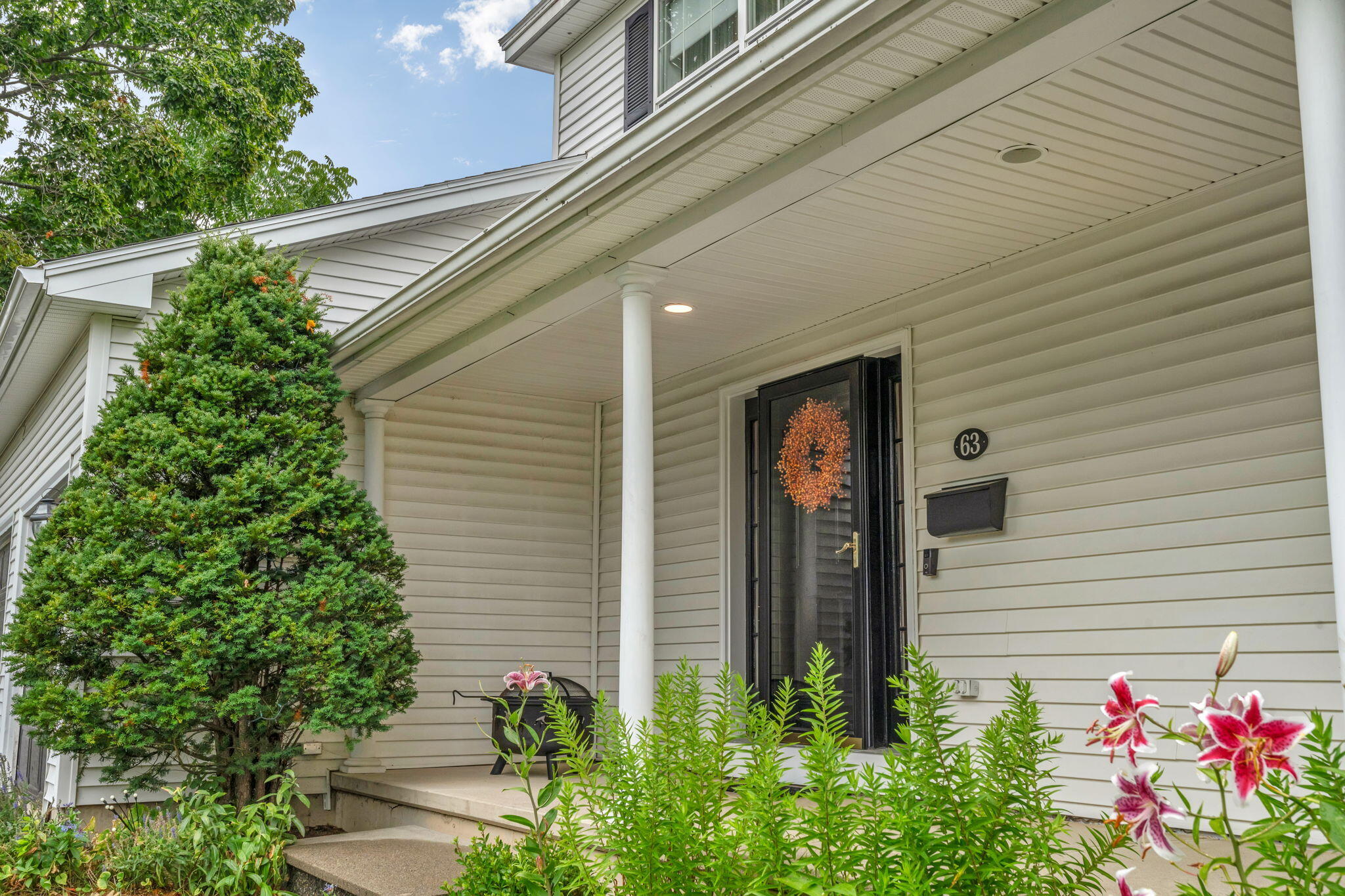 Front entrance with a covered porch, black storm door, white columns, and flowering garden plants.