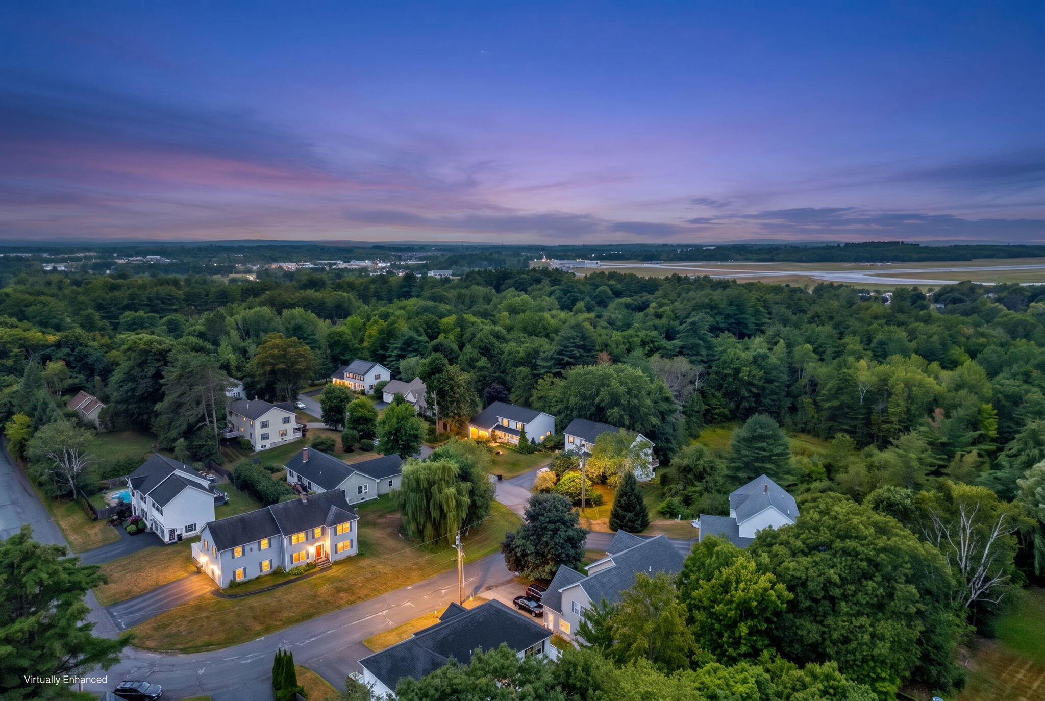 Aerial view of homes among trees at dusk, with an airport runway on the horizon.