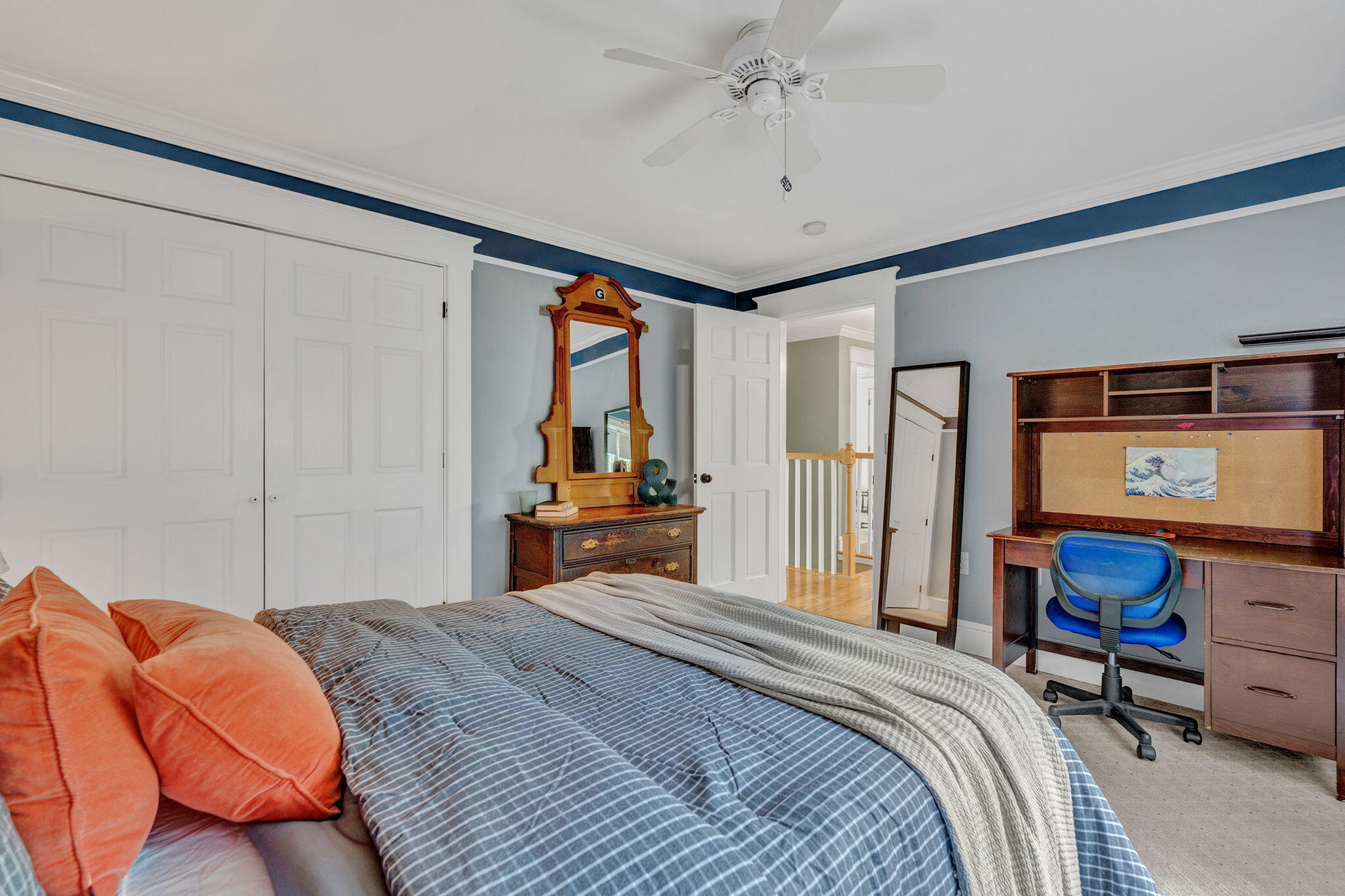 Bedroom with a large bed, built-in closets, wooden desk, and antique dresser with mirror.