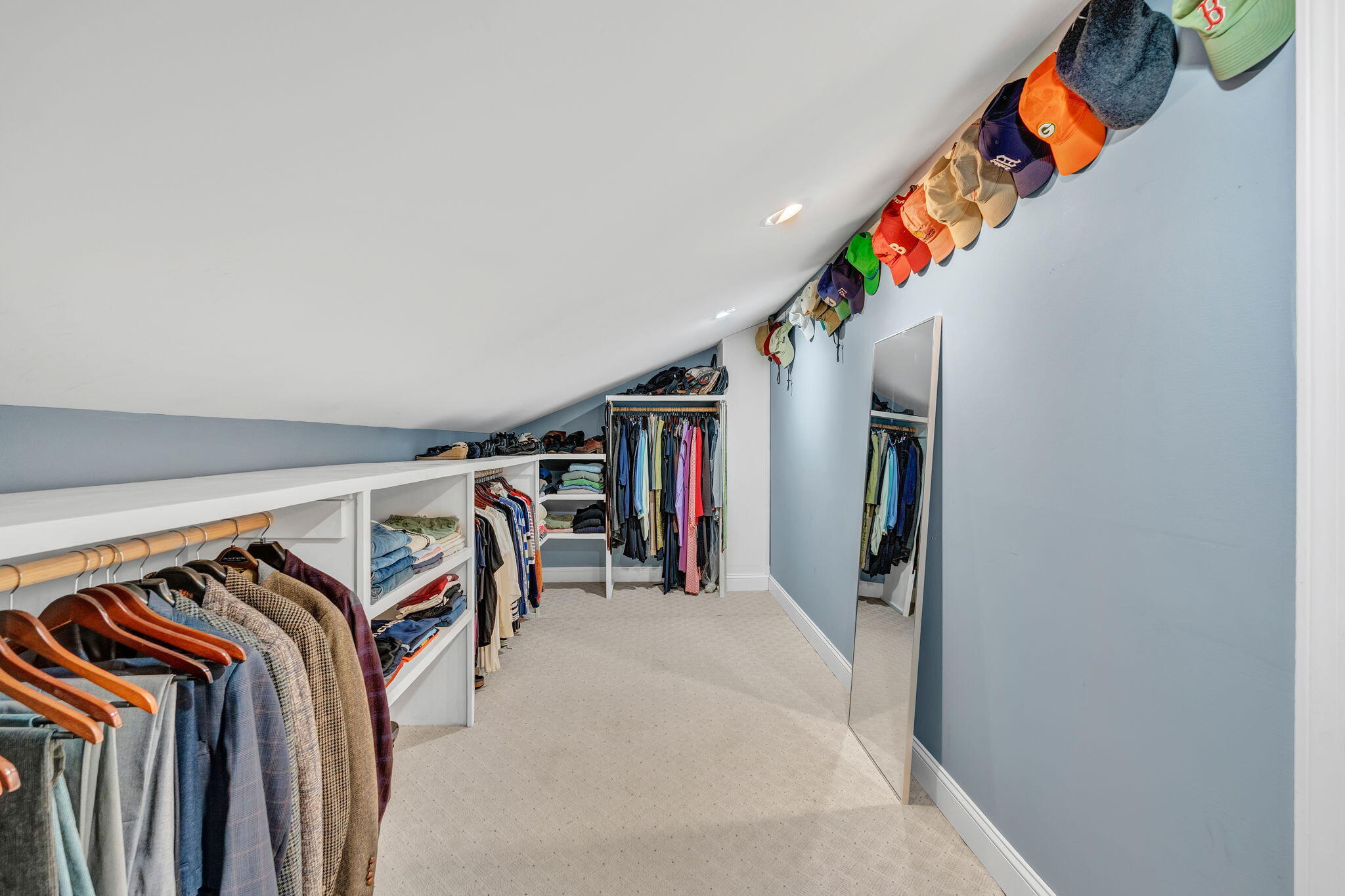 Walk-in closet with built-in clothing shelves, hats displayed along the ceiling, and a full-length mirror.