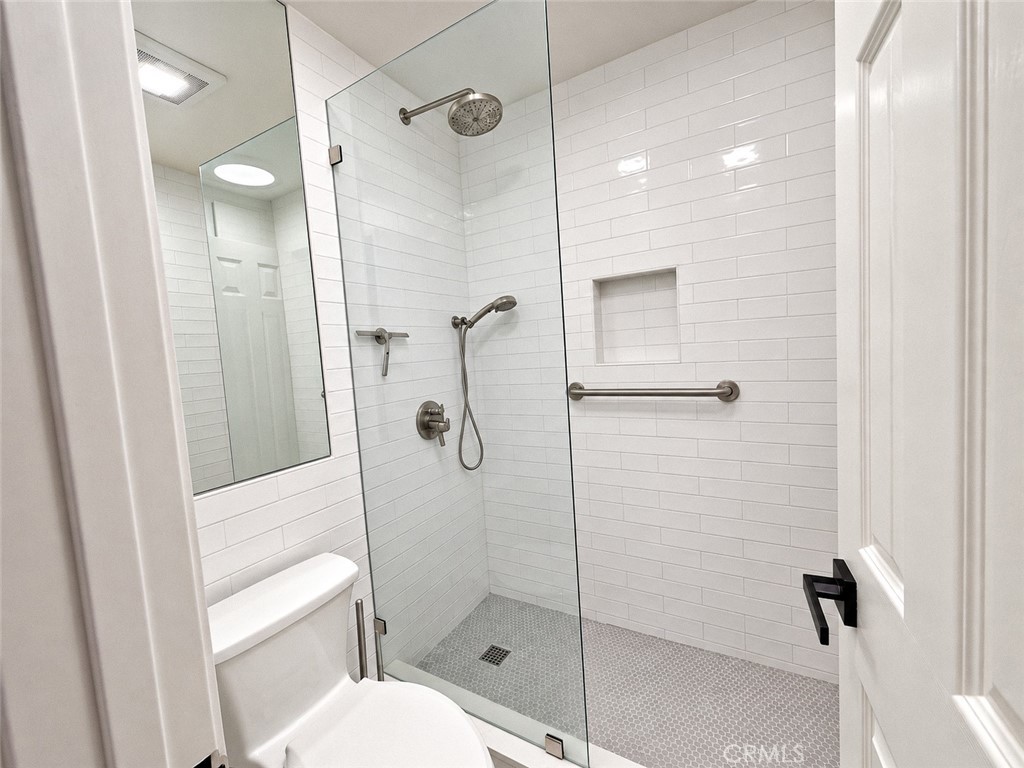 Bathroom with a glass walk-in shower, white subway tile, grab bars, and a handheld showerhead.