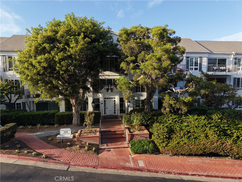 Two-story residential building with a central brick entry, mature trees, and landscaped frontage.