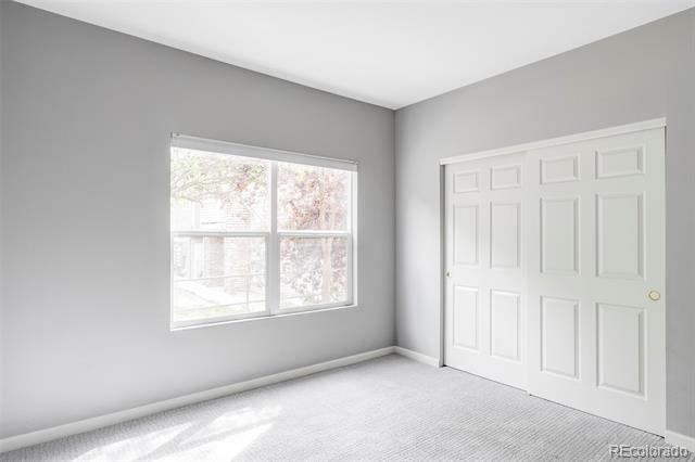Empty carpeted room with a large window and white paneled closet doors.