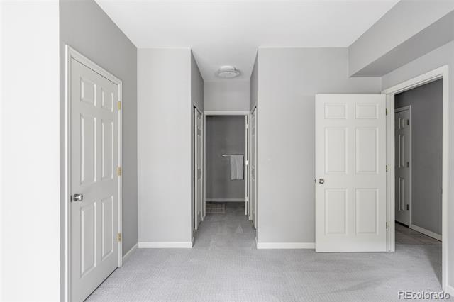 Empty carpeted room with white walls, open doors to adjoining spaces, and a ceiling light.
