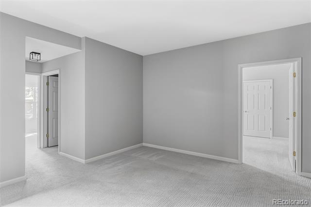 Empty gray-carpeted room with gray walls and open doorways to adjoining spaces.