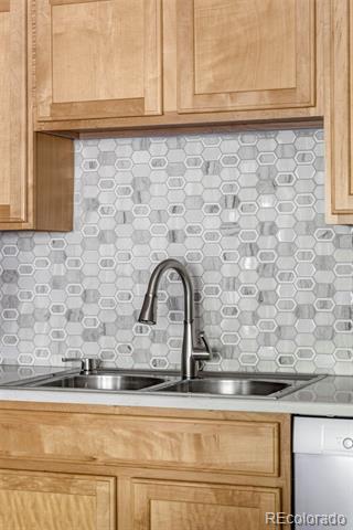 Kitchen with light wood cabinets, hexagonal tile backsplash, double-basin sink, and dishwasher.