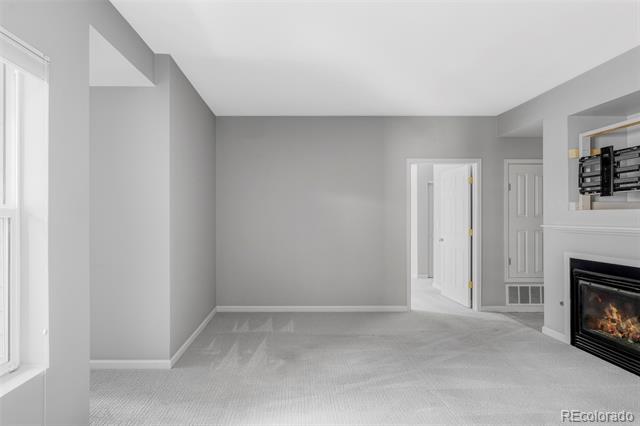 Empty living room with gray carpet, a fireplace, and a bright window.