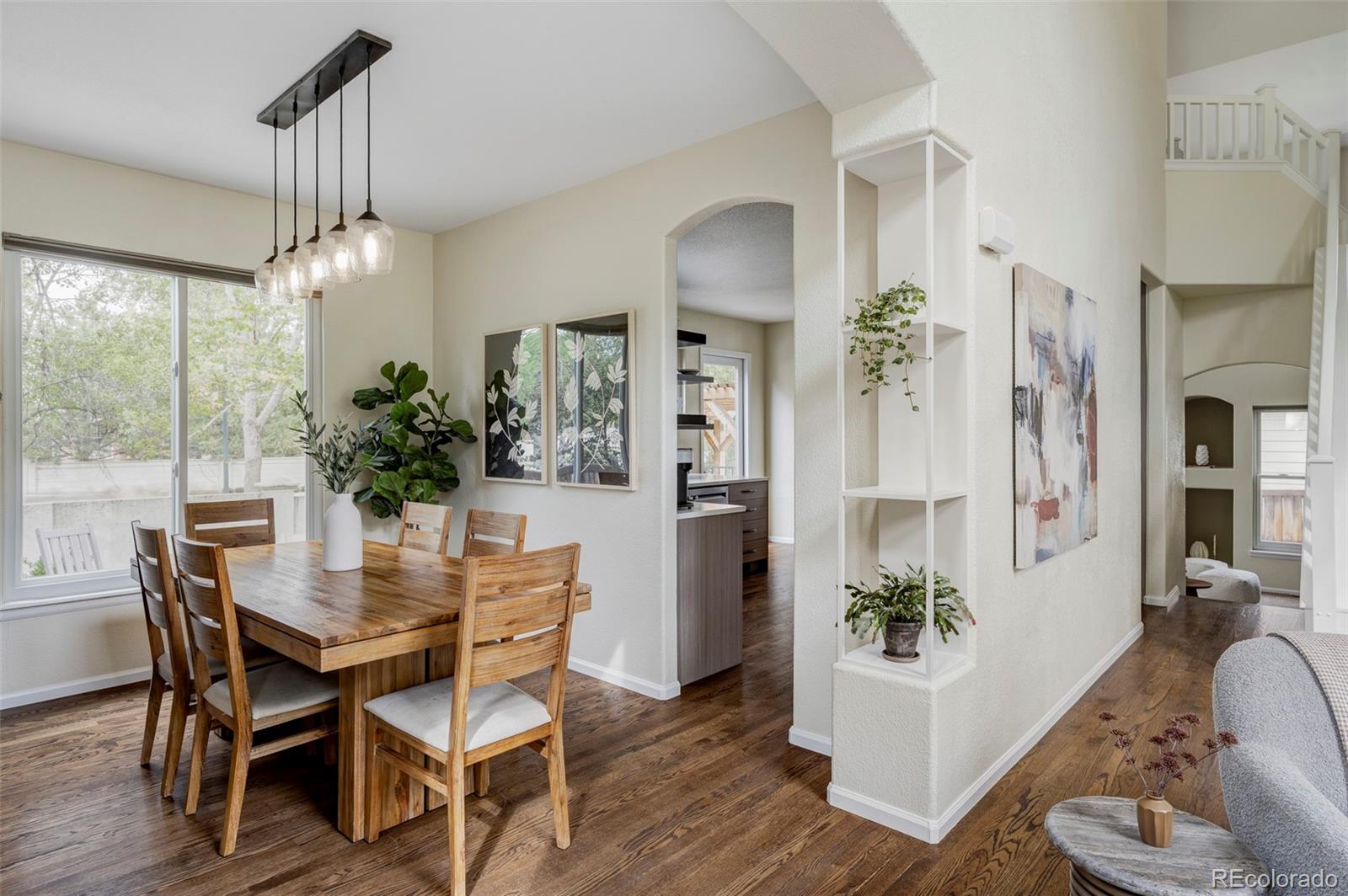 Dining room with a wooden table, glass pendant lights, and an arched opening to the kitchen.