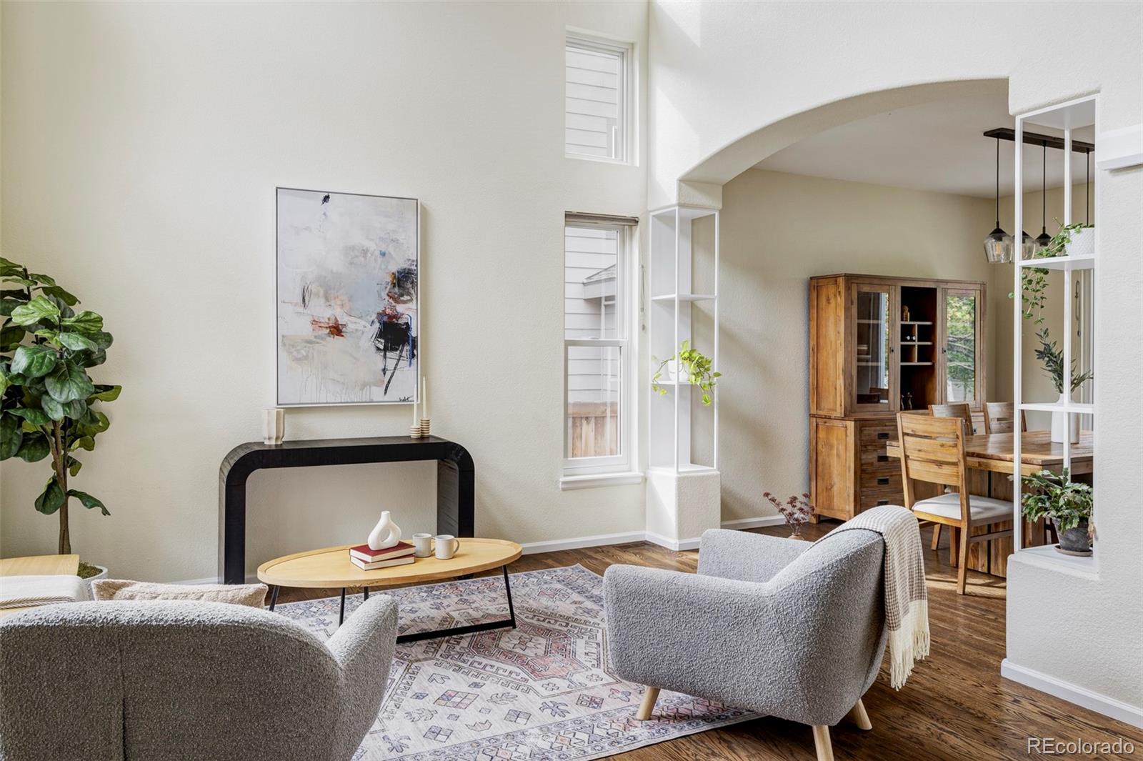 Bright living room with gray armchairs, patterned rug, and an arched opening to the dining area.
