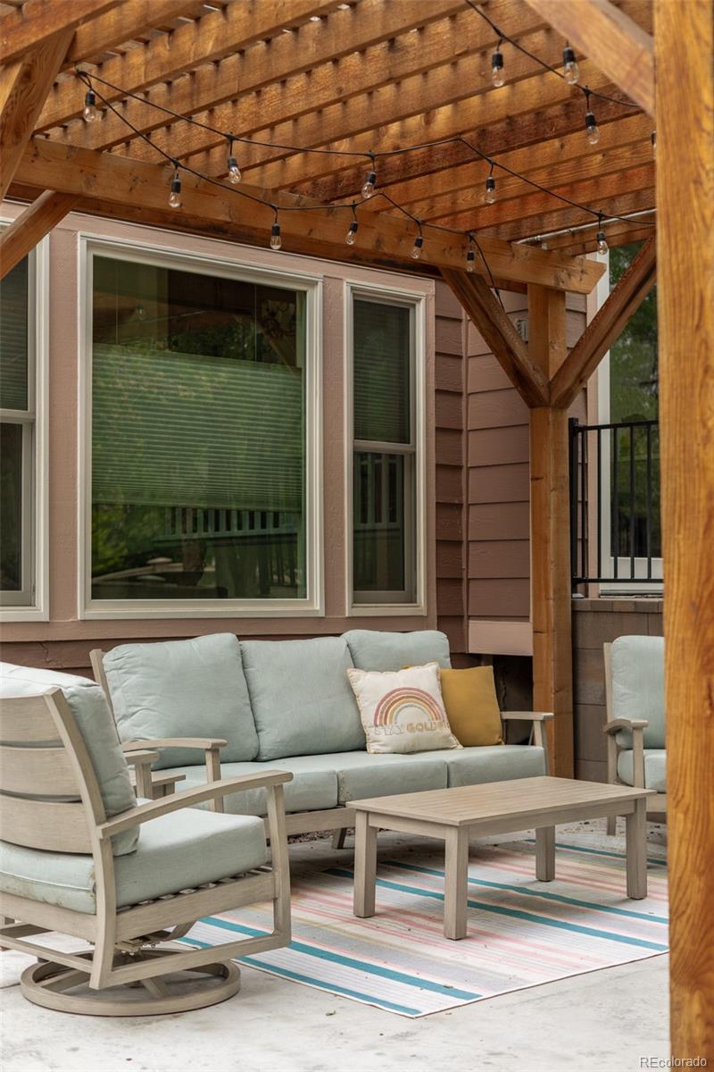Patio seating beneath a timber pergola with string lights and a striped rug.