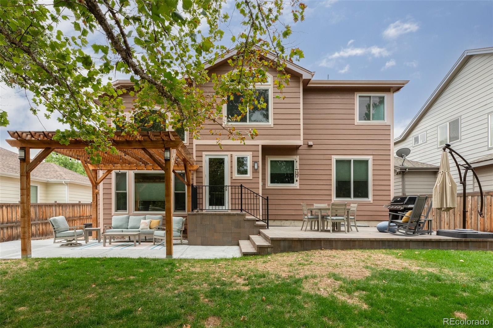 Rear of a two-story home with a pergola-covered seating area and spacious patio.