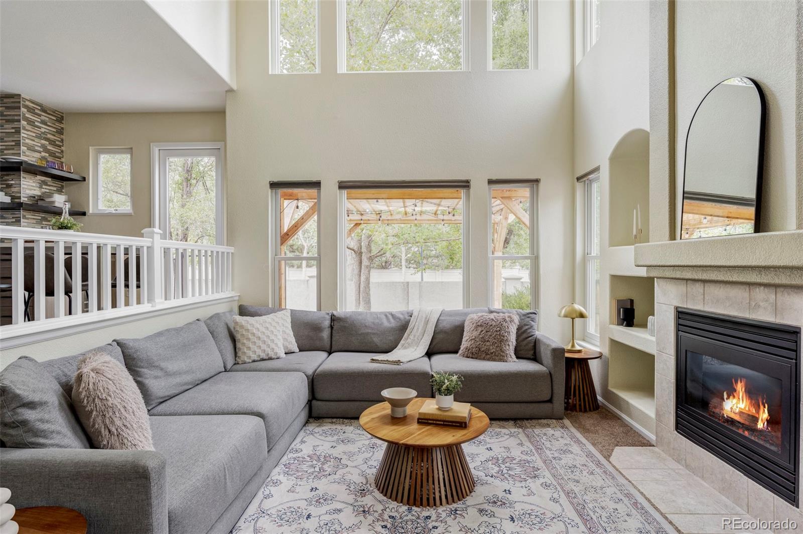Living room with a gray sectional, tall windows, and a tiled fireplace.