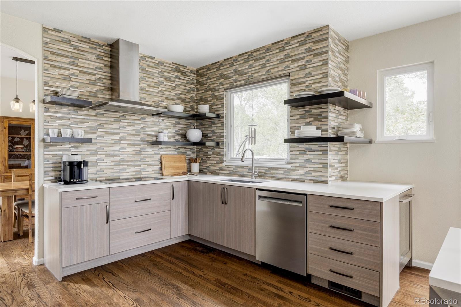 Modern kitchen with multicolored tile backsplash, open shelves, and gray cabinetry.
