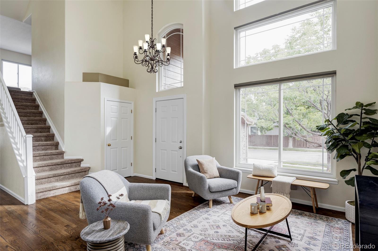 Staged living room with a vaulted ceiling, tall windows, and staircase.