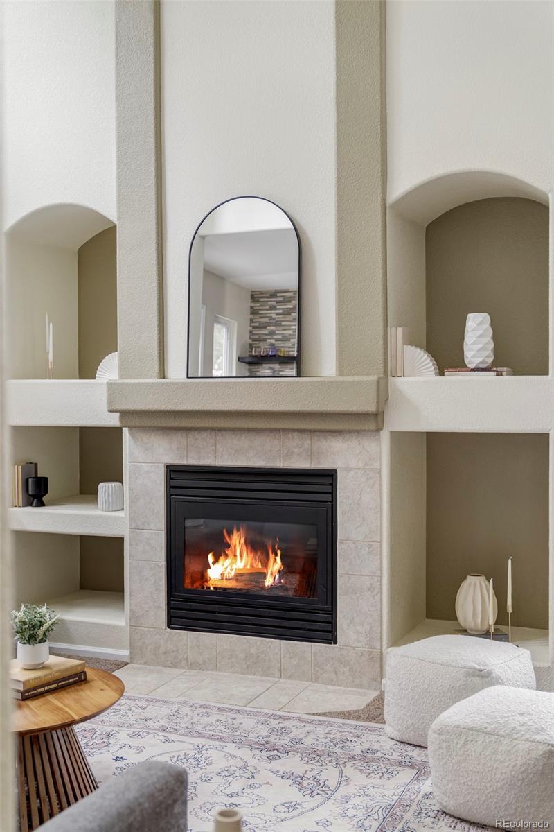 Living room with a lit fireplace, tiled surround, built-in niches, and an arched mirror.