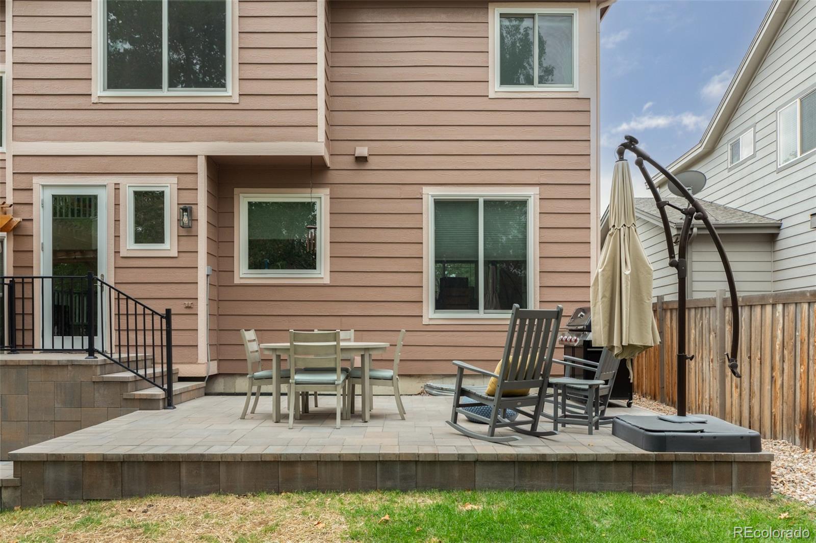 Raised stone patio behind a two-story home, furnished with outdoor dining and lounge seating.