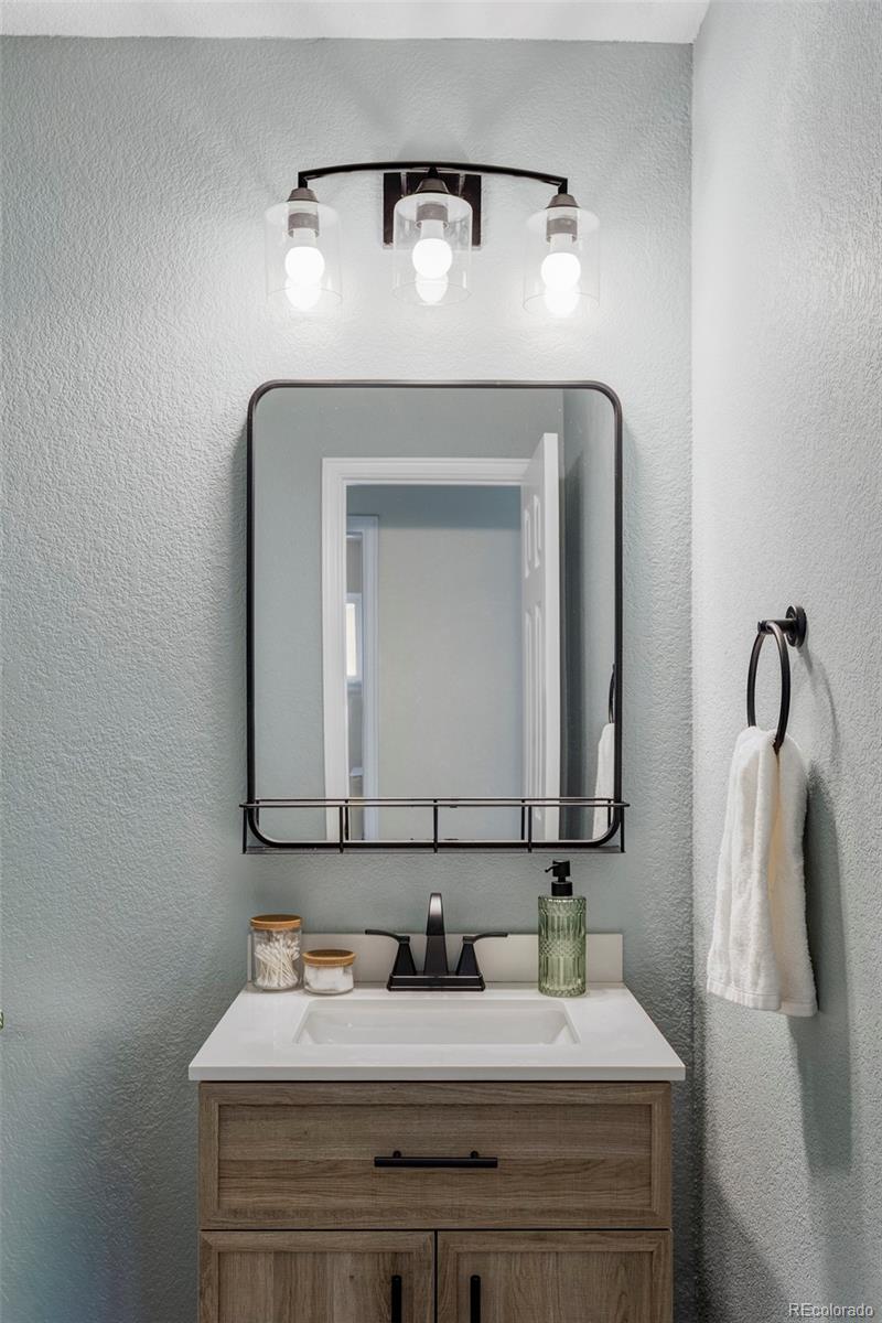 Bathroom vanity with wood-grain cabinetry, a black-framed mirror, and three-light fixture.
