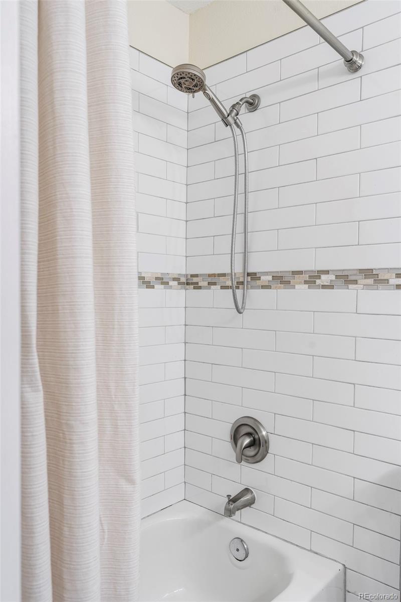 Bathroom tub and shower with white subway tile and a handheld showerhead.