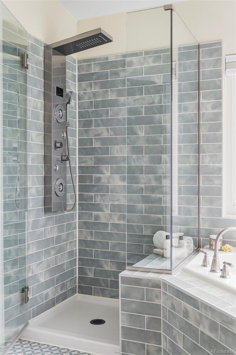 Tiled bathroom shower with glass enclosure, rainfall showerhead, and multi-jet shower panel.