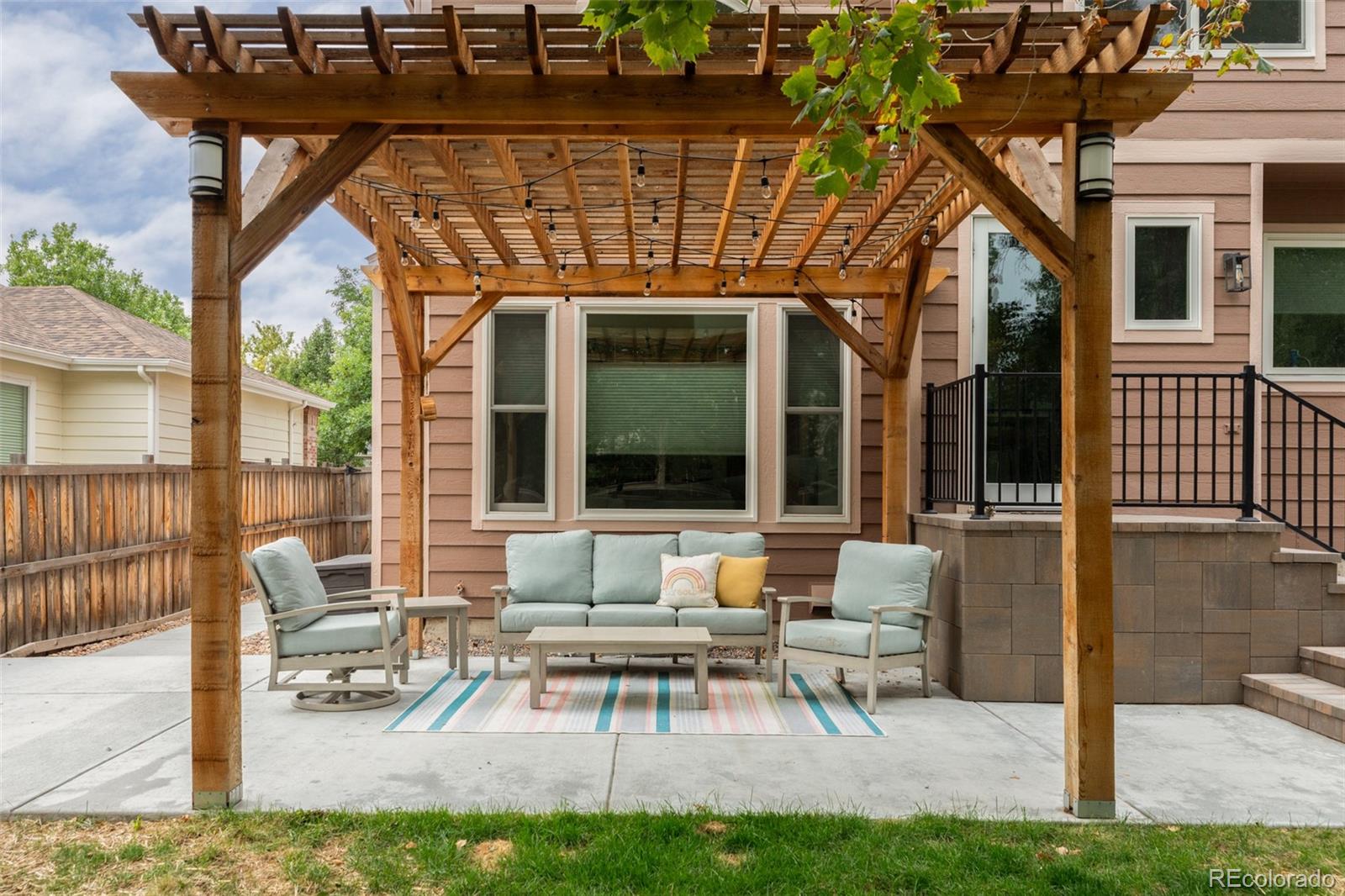 Backyard patio with a wood pergola, string lights, and cushioned seating beside the home.