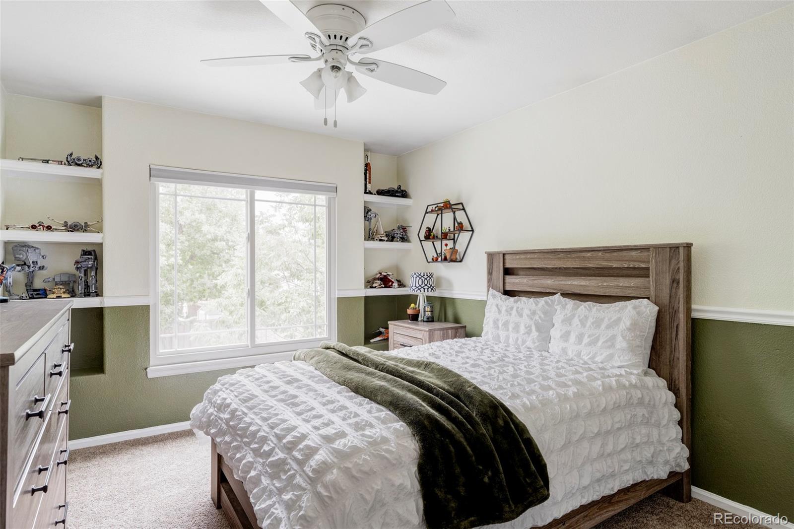Bedroom with a white-bedded bed, built-in display shelves, and a wide window.