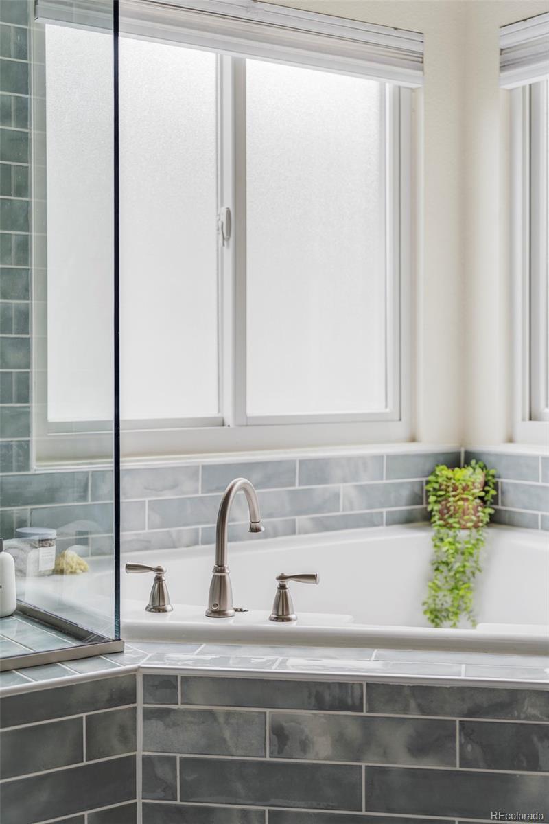Corner bathtub beneath large windows, surrounded by gray tile and a glass shower enclosure.