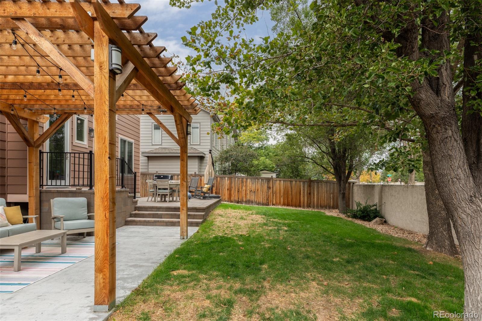 Backyard with a wood pergola, furnished patio, fenced lawn, and mature trees.