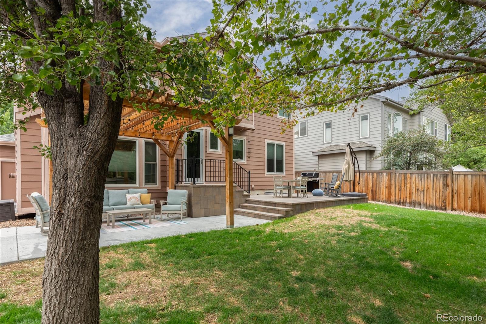 Home’s backyard patio with a wooden pergola, outdoor seating, raised deck, and mature shade trees.