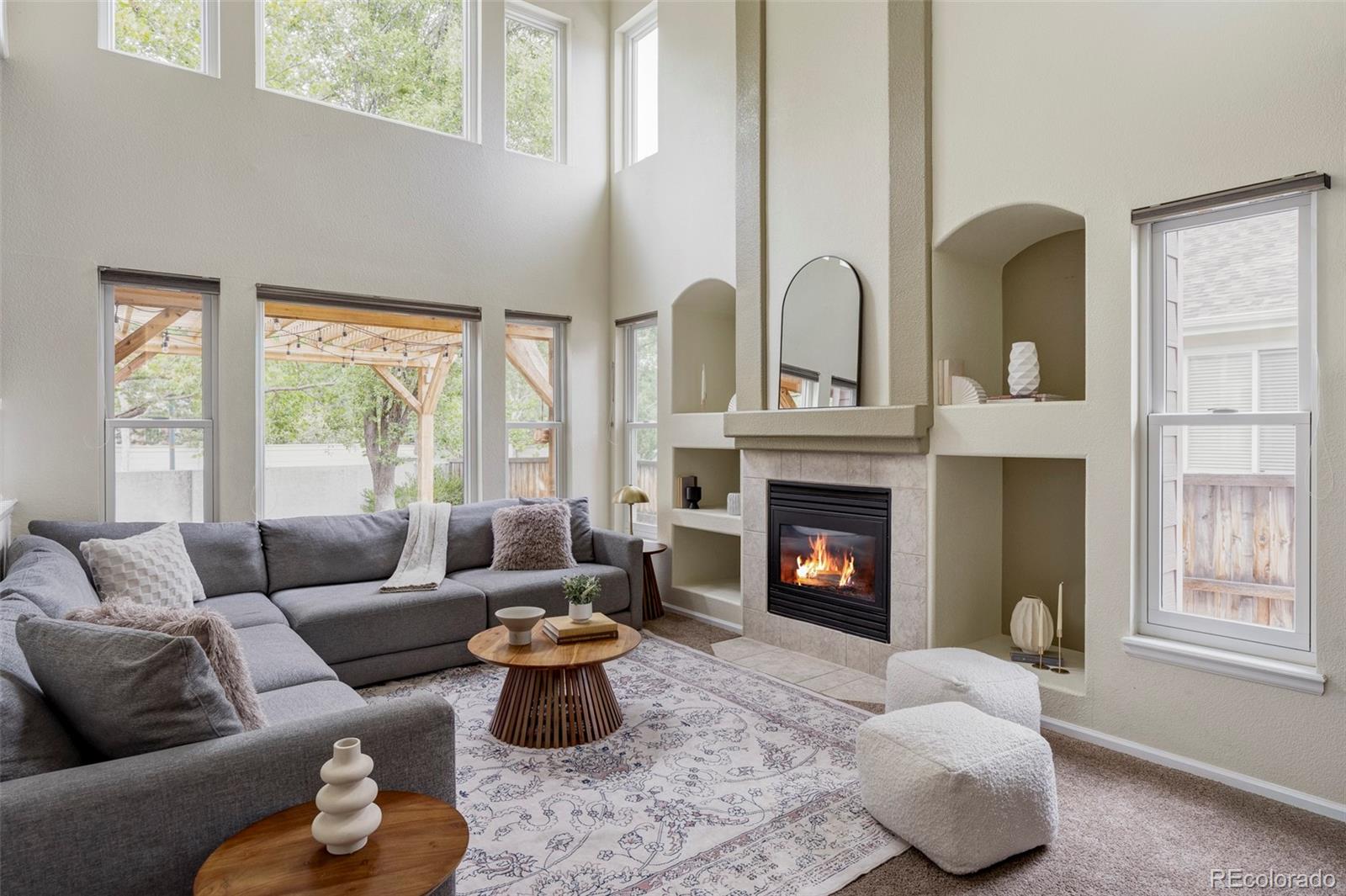 Living room with a vaulted ceiling, gray sectional, large windows, and a lit fireplace.
