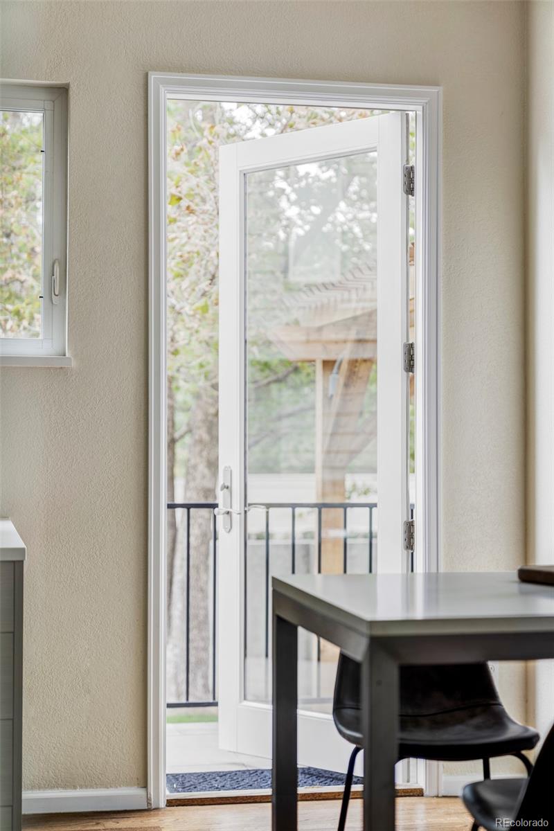 Dining area with dark table beside an open glass door to a tree-lined balcony.