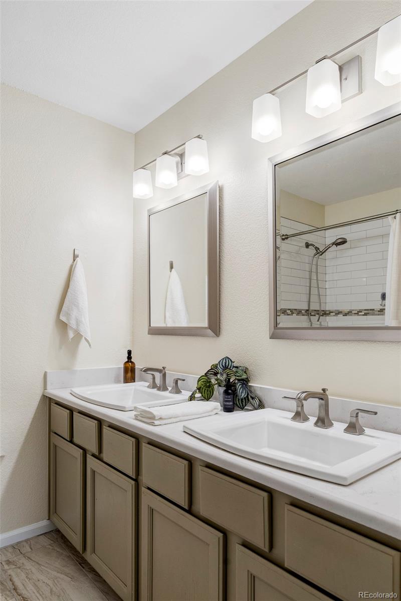 Bathroom with a double-sink vanity, taupe cabinets, and a tiled shower reflected in the mirror.