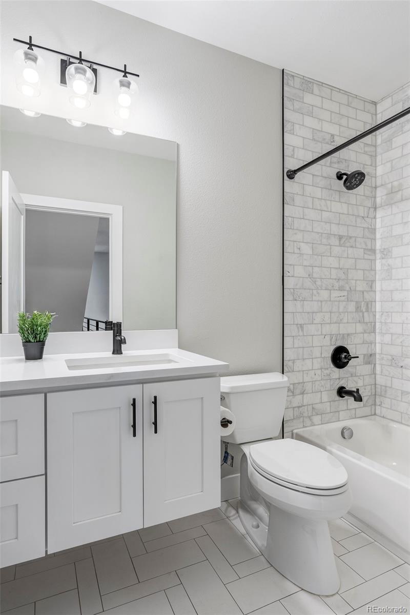 Bathroom with a white vanity and marble-look tiled tub surround with black fixtures.