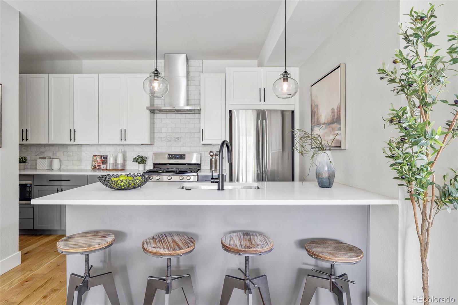 Kitchen with a large white island, four stools, stainless steel appliances, and a marble-tile backsplash.