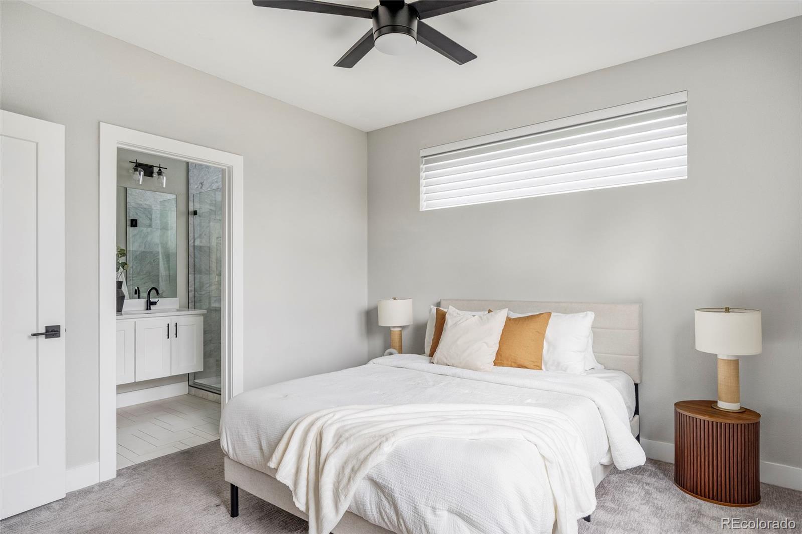 Staged bedroom with a white bed and mustard pillow, opening to an en suite bathroom.