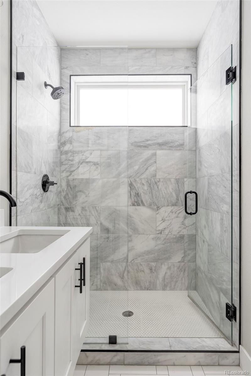 Bathroom with a glass shower, gray-veined tile, high window, and white vanity.