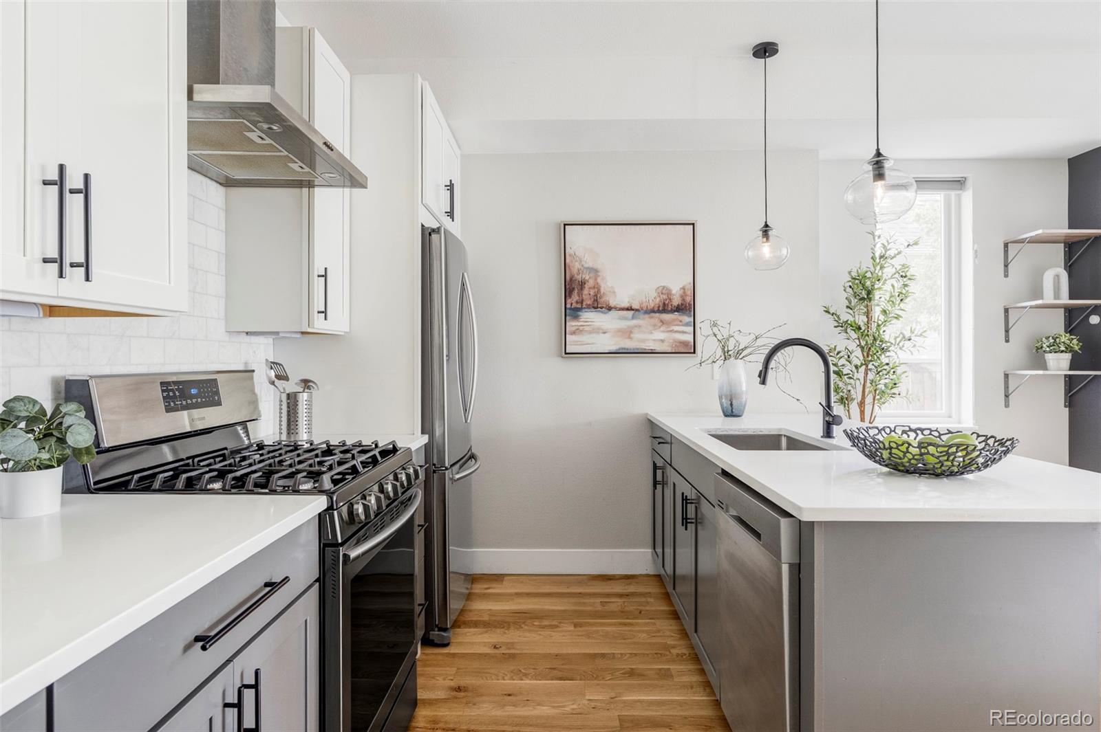 Modern kitchen with a long white island, undermount sink, stainless steel appliances, and wood flooring.