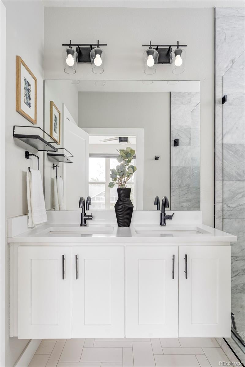 Bathroom with a white double vanity, black fixtures, large mirror, and marble-tiled shower.