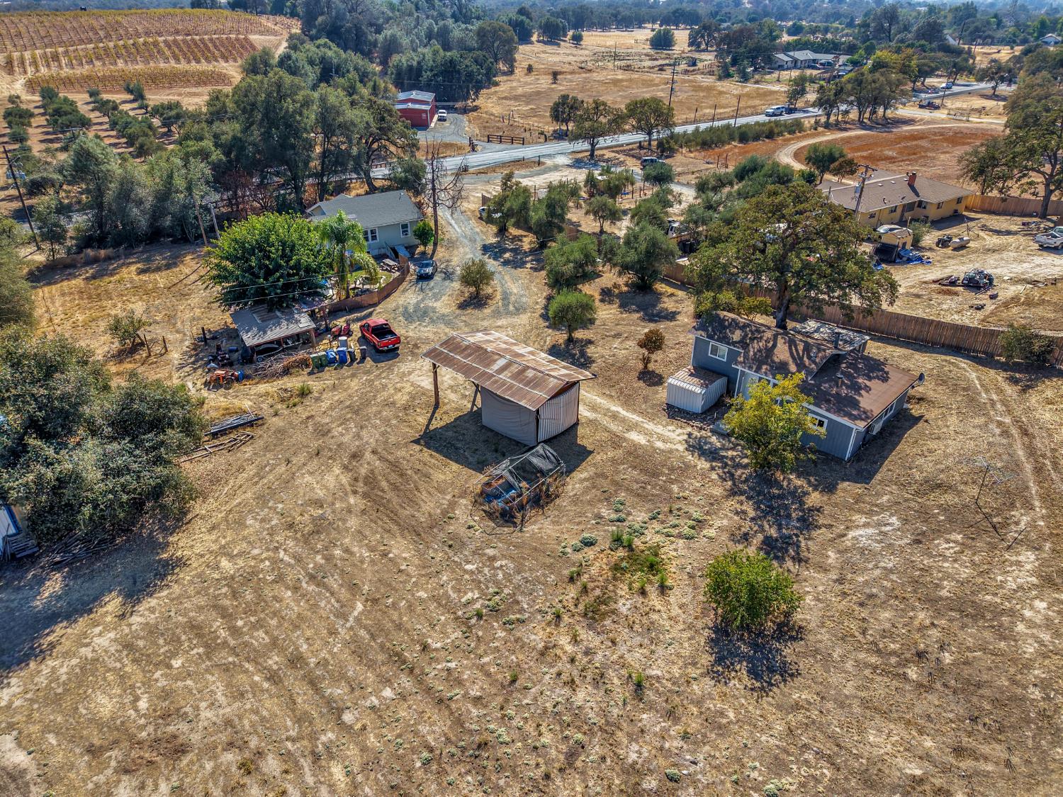 Aerial view of a rural property with homes, outbuildings, dry open land, and nearby vineyards.
