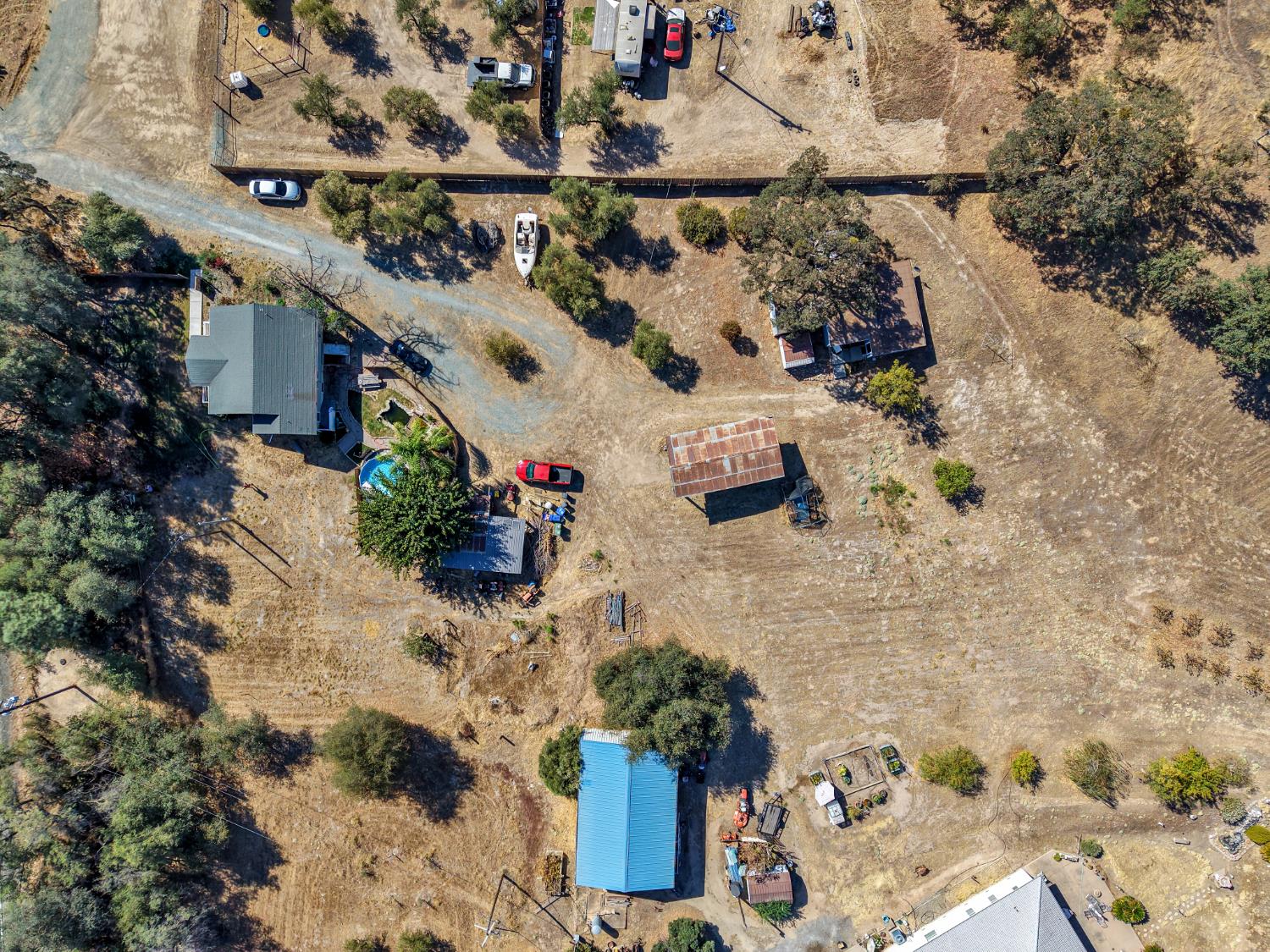 Aerial view of a rural property with several outbuildings, a swimming pool, and dry open land.