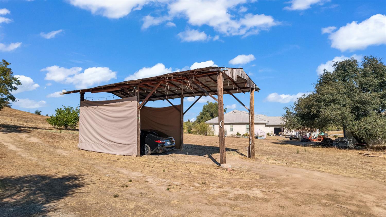 Open-sided wooden carport with a corrugated roof and a car, with the house in the background.