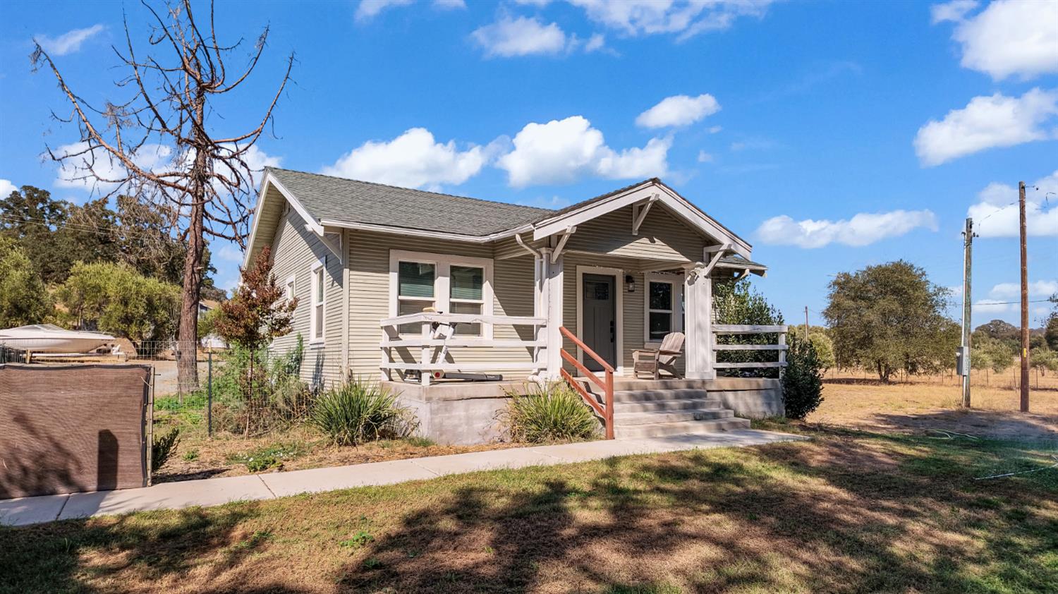 Small gray house with a covered front porch, white railings, and concrete steps.