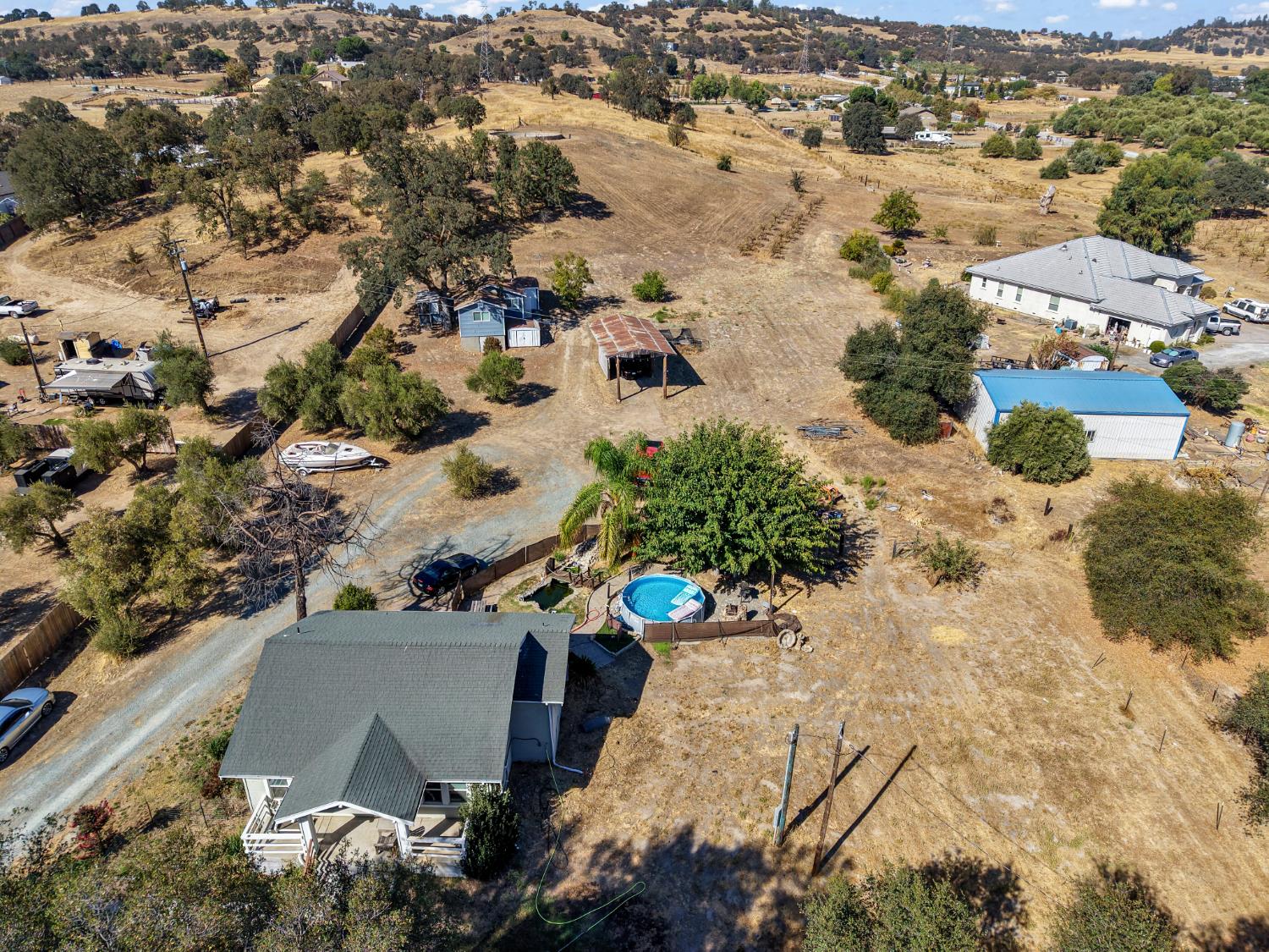 Aerial view of a rural property with a house, outbuildings, a pool, and dry open land.