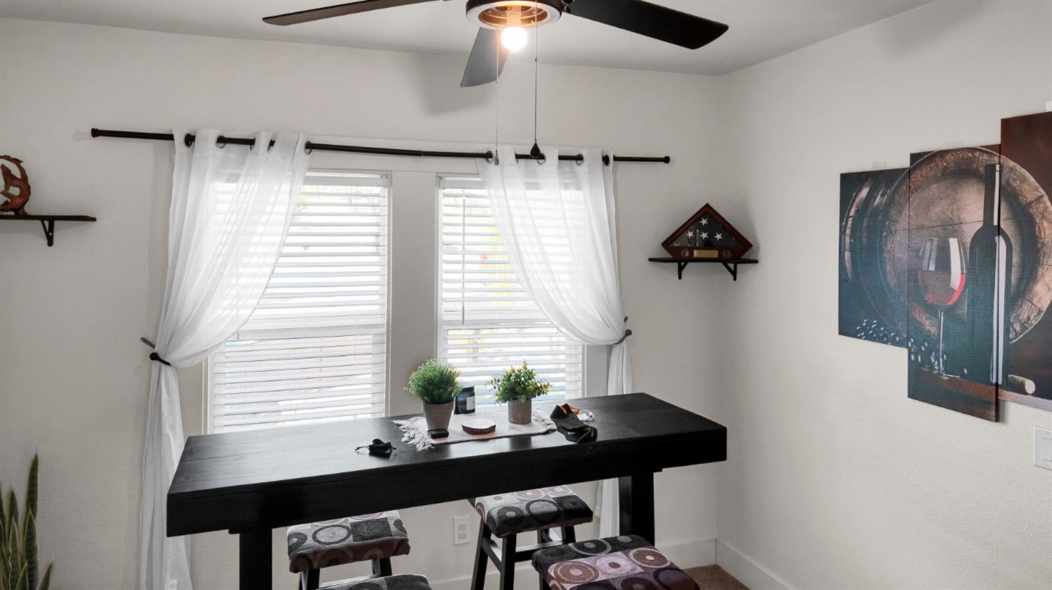 Dining area with a black table, patterned stools, and bright shuttered windows.