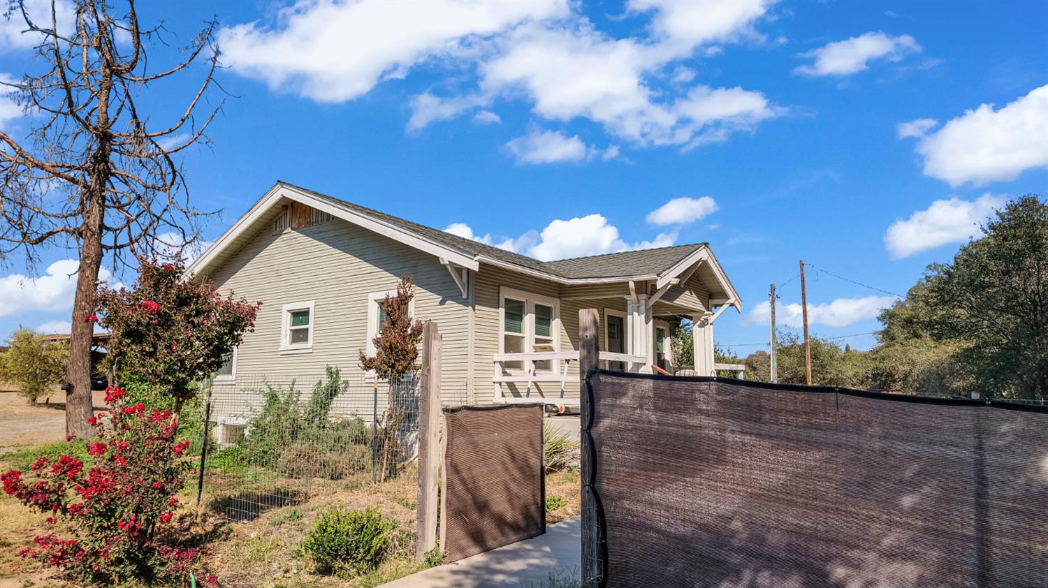 Single-story beige house with a covered porch, mesh fencing, and red rose bushes.