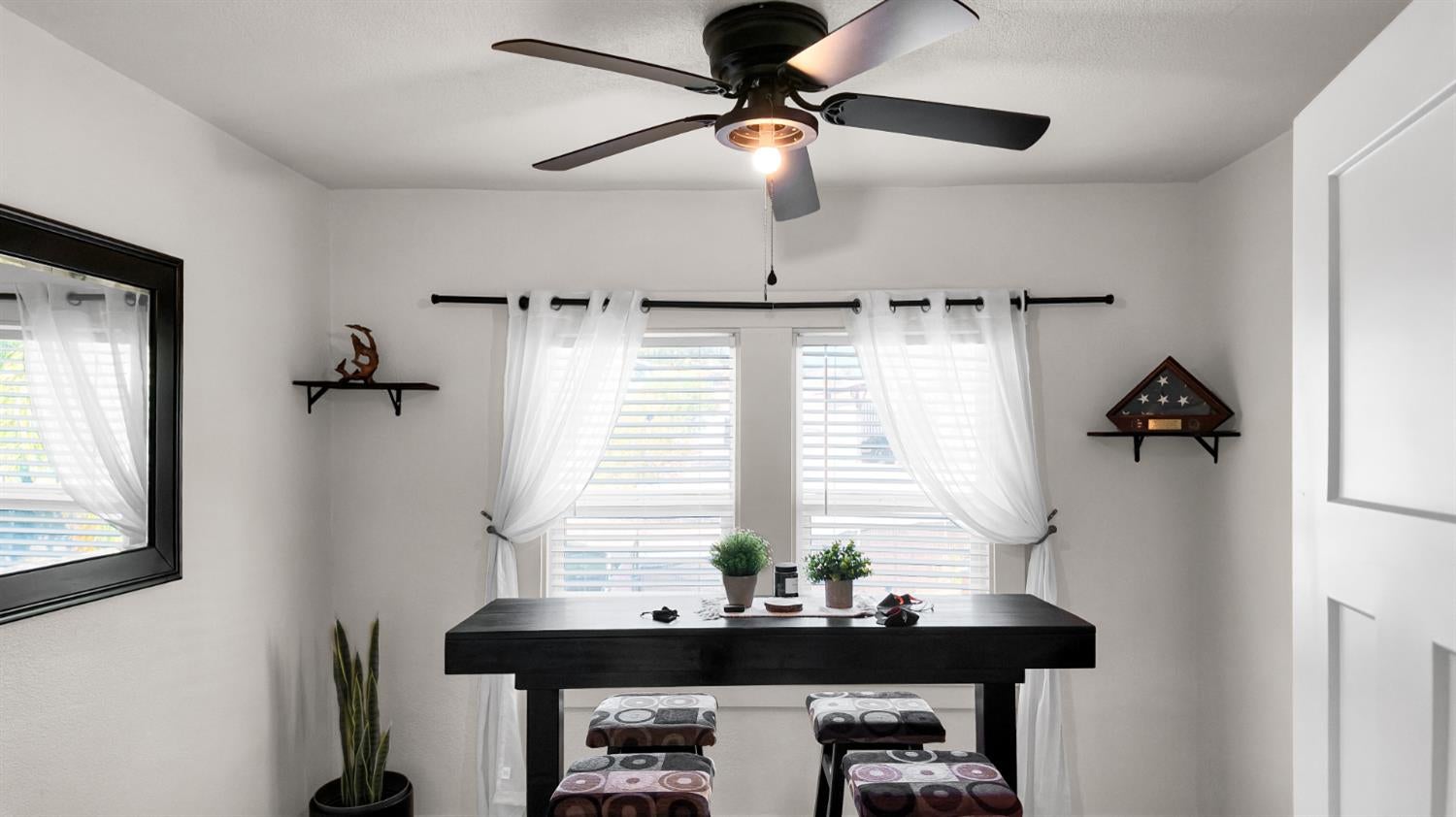 Dining area with a tall black table, patterned stools, and bright curtained windows.