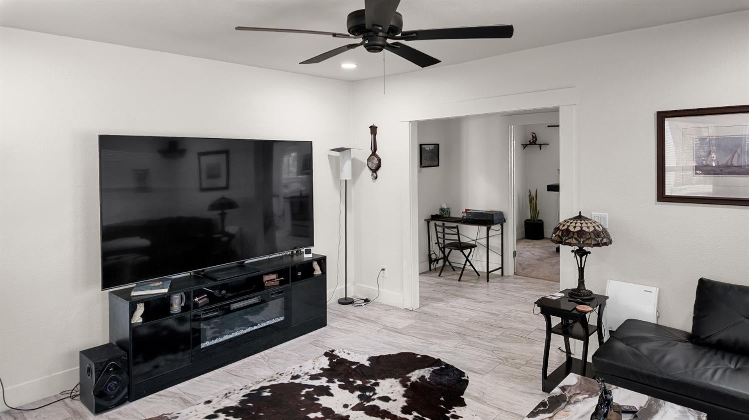 Living room with a large TV, black media console, leather sofa, and light tile flooring.