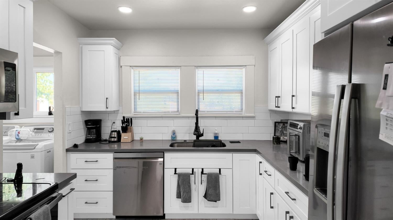 Kitchen with white shaker cabinets, gray countertops, and a sink beneath two windows.