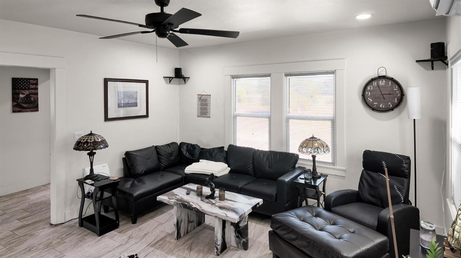 Living room with a black leather sectional, matching recliner, marble-look coffee table, and ceiling fan.