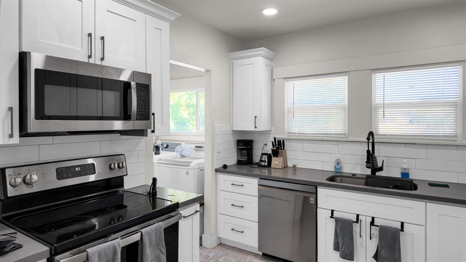 Bright kitchen with white cabinets, stainless steel appliances, and a laundry area visible through the doorway.